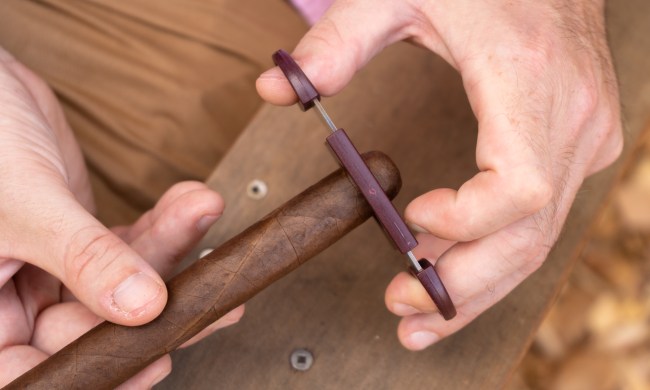 Close-up of hands cutting a cigar with a cigar cutter.