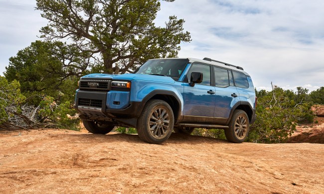 A blue 2024 Toyota Land Cruiser parked on a rocky rise with sparse vegetation in the background.